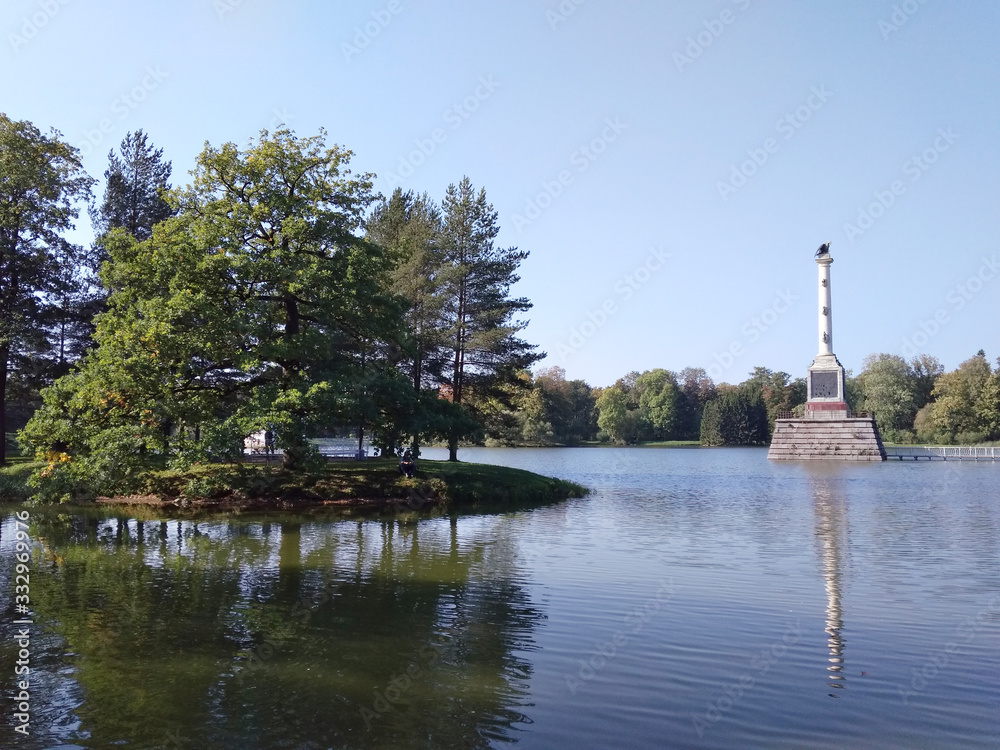 Summer sunny park with a lawn by the lake with column  in the middle of the lake