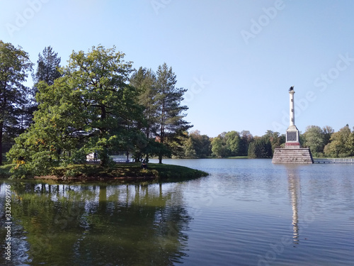 Summer sunny park with a lawn by the lake with column in the middle of the lake