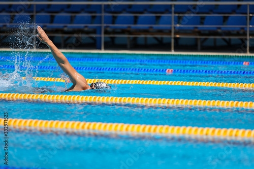 Athletic man swimming in front crawl style in the swimming pool with clear blue water.