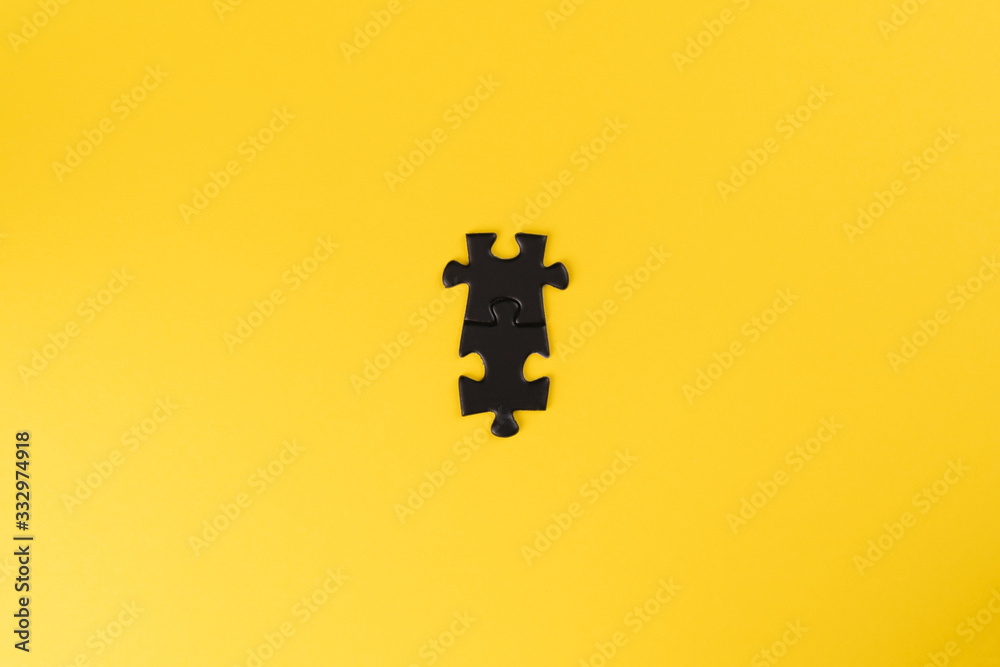 Two connected black puzzle pieces on a yellow background. The pieces in the centre of the frame Two connected black puzzle pieces on a yellow background. The pieces in the centre of the frame