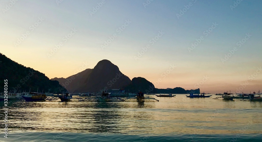 Sunset with outrigger boats before vanilla sky at El Nido beach, with islands in background, El Nido, Palawan, Philippines