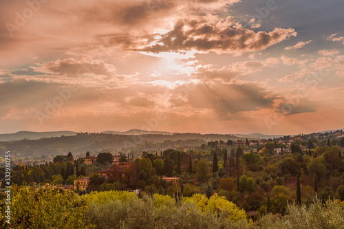 Classic Tuscany landscape with the mid-afternoon sun and its rays illuminating the green hills, cypresses, pines and villas