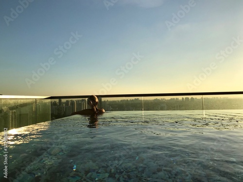 Blond woman in rooftop pool on skyscraper, with skyline in background, Singapore, South East Asia