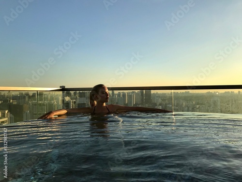 Blond woman in rooftop pool on skyscraper, with skyline in background, Singapore, South East Asia © HWL Photos