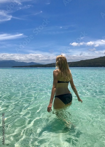 Blond woman from behind walking in the water, in bay with green and blue water, Cebu Island, Philippines
