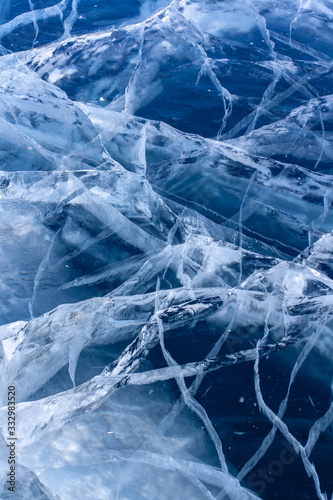Natural texture of clear blue ice with deep cracks. Beautiful cracks in the clear ice of the lake. Vertical.