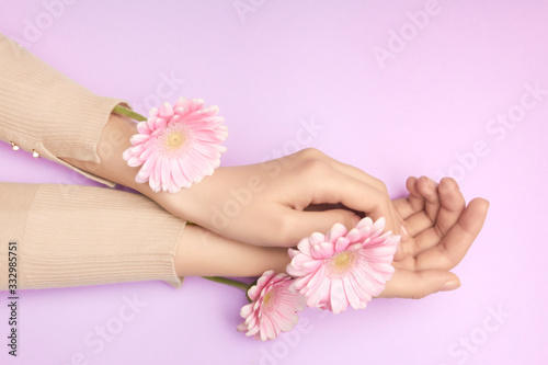 Pink petals of a flower in gentle womans hands on a violet background. Concept of advertisment of beauty salon. A thin wrist and natural manicure.