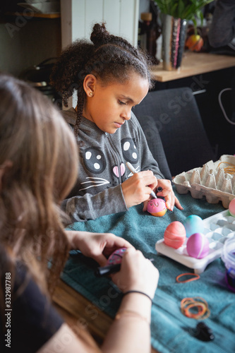 Pretty mixed child decorating an easter egg with a marker and plastic template. photo