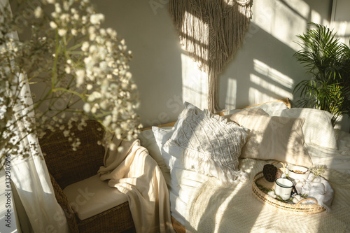 Cozy boho style sunny bedroom with light and shadows and close up of white gypsophila flowers. Authentic real life interior photo