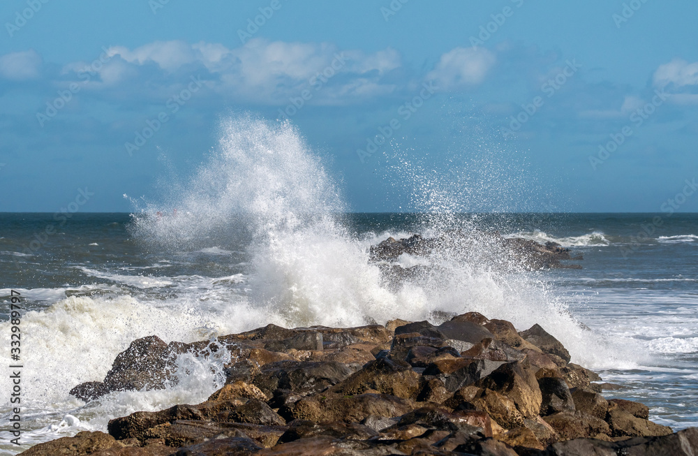 Waves breaking over a rock jetty wall.