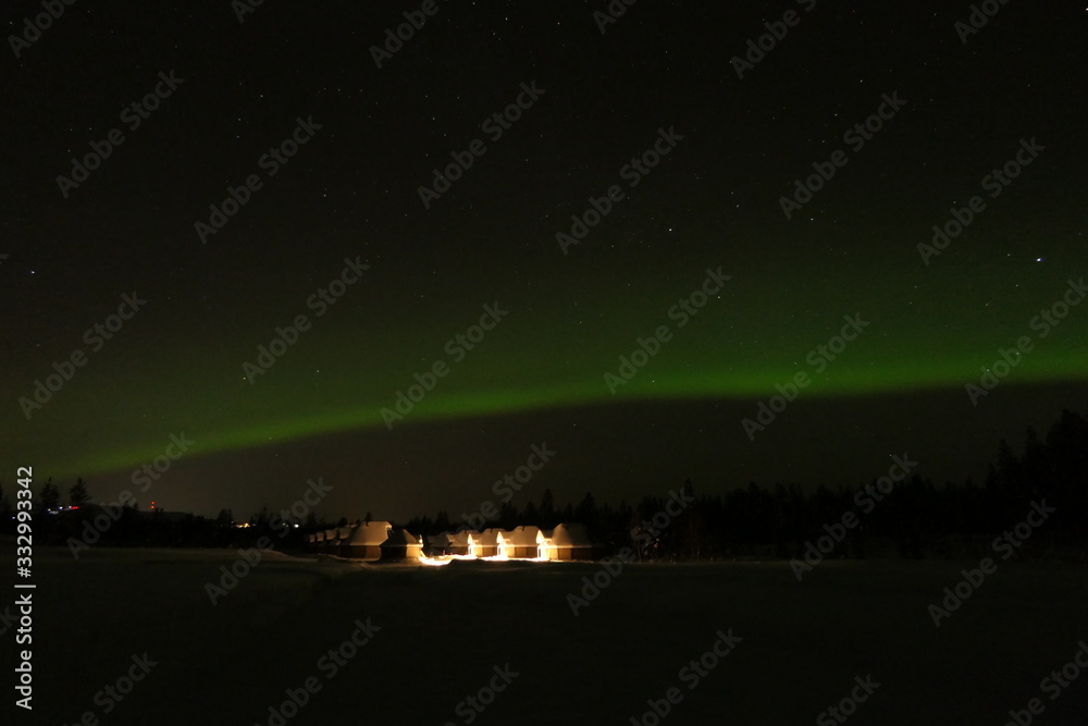 Green aurora borealis at night in snow landscape and cottages in background, Lapland, Finland