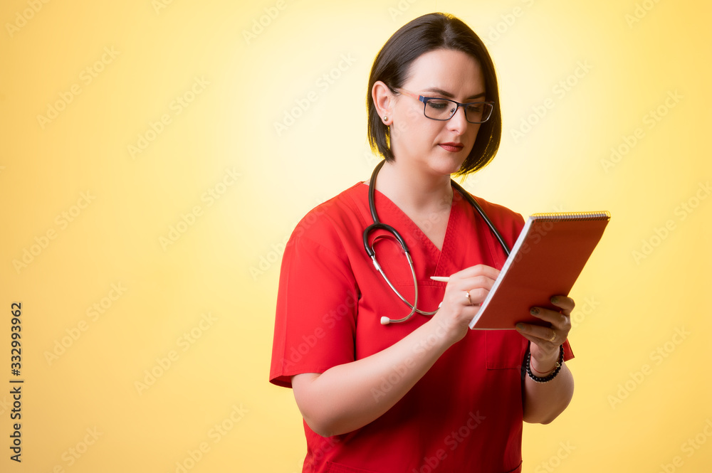Beautiful woman doctor with stethoscope, wearing red scrubs takes notes Beautiful woman doctor with stethoscope, wearing red scrubs takes notes