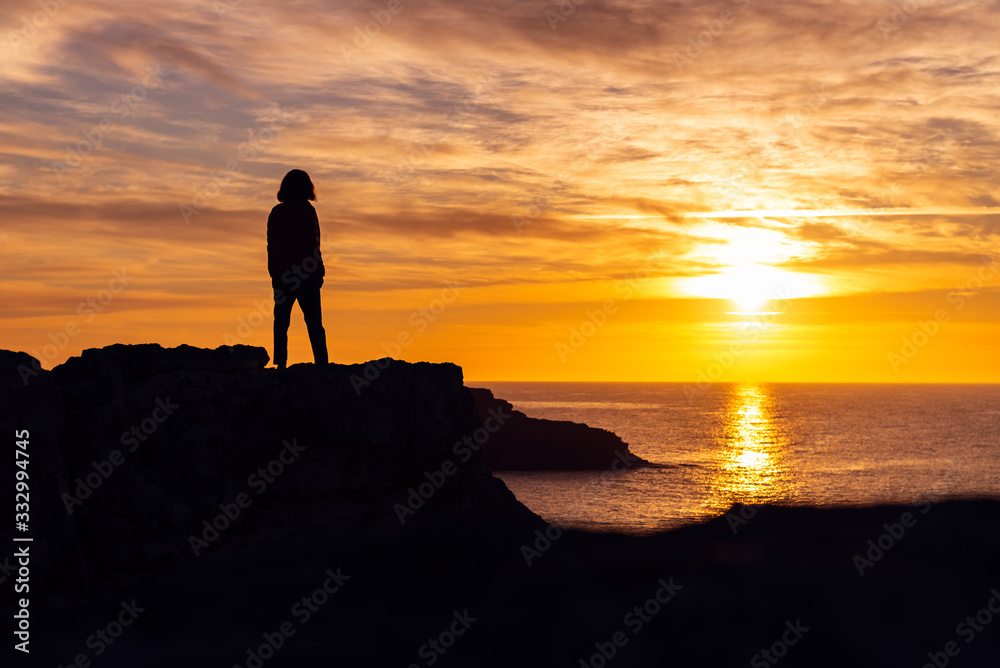 Silhouette of young woman on the edge of the cliff with sea view during sunrise. Holidays and enjoying life concept