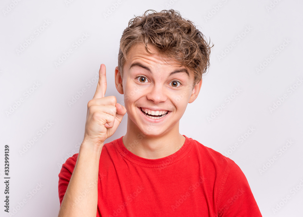 Portrait of smiling teen boy pointing a great idea, on grey background. Awesome idea. Beautiful young teenager keeping finger up, looking at camera. Happy cute child have unexpected idea. Portrait of smiling teen boy pointing a great idea, on grey background. Awesome idea. Beautiful young teenager keeping finger up, looking at camera. Happy cute child have unexpected idea.