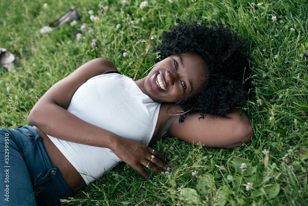 Smiling african girl is laying on the grass in jeans and white crop top. Smiling african girl is laying on the grass in jeans and white crop top.