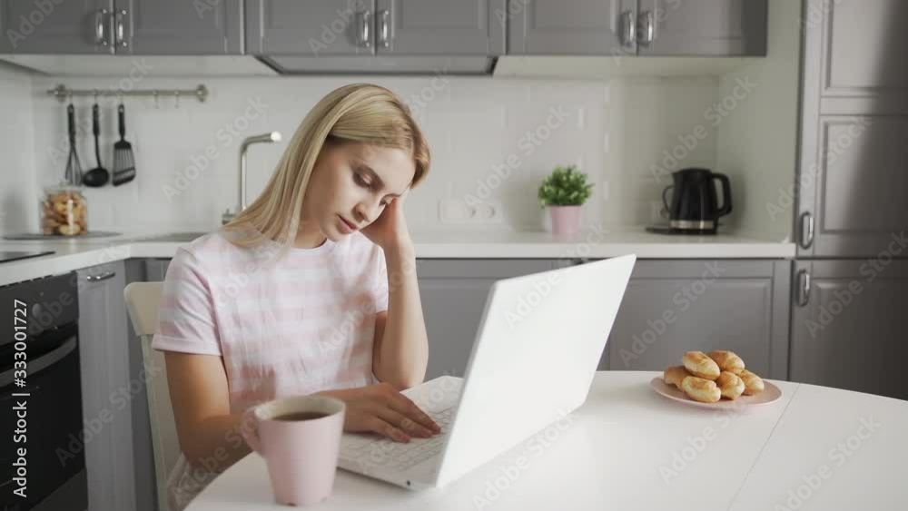 Thoughtful woman drinking a coffee and using laptop computer at kitchen. Business woman working on notebook Thoughtful woman drinking a coffee and using laptop computer at kitchen. Business woman working on notebook
