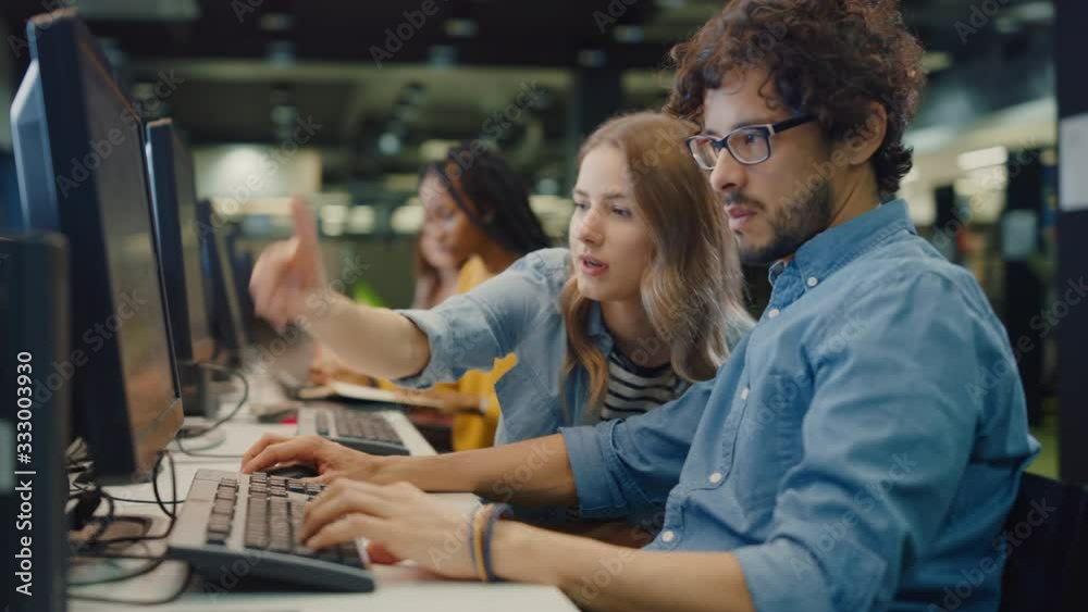 University Library: Bright Caucasian Girl and Smart Boy Together Work on Computers, Chat, Discuss Class Assignment, Explain and Advice Each Other. Diverse Group of Students Exam Study Teamwork