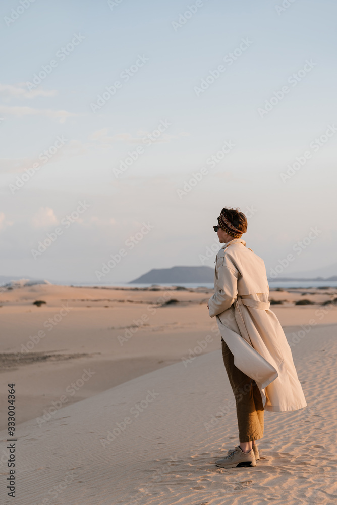 Stylish woman in beige trench coat standing on sandy hill. Stylish woman in beige trench coat standing on sandy hill.