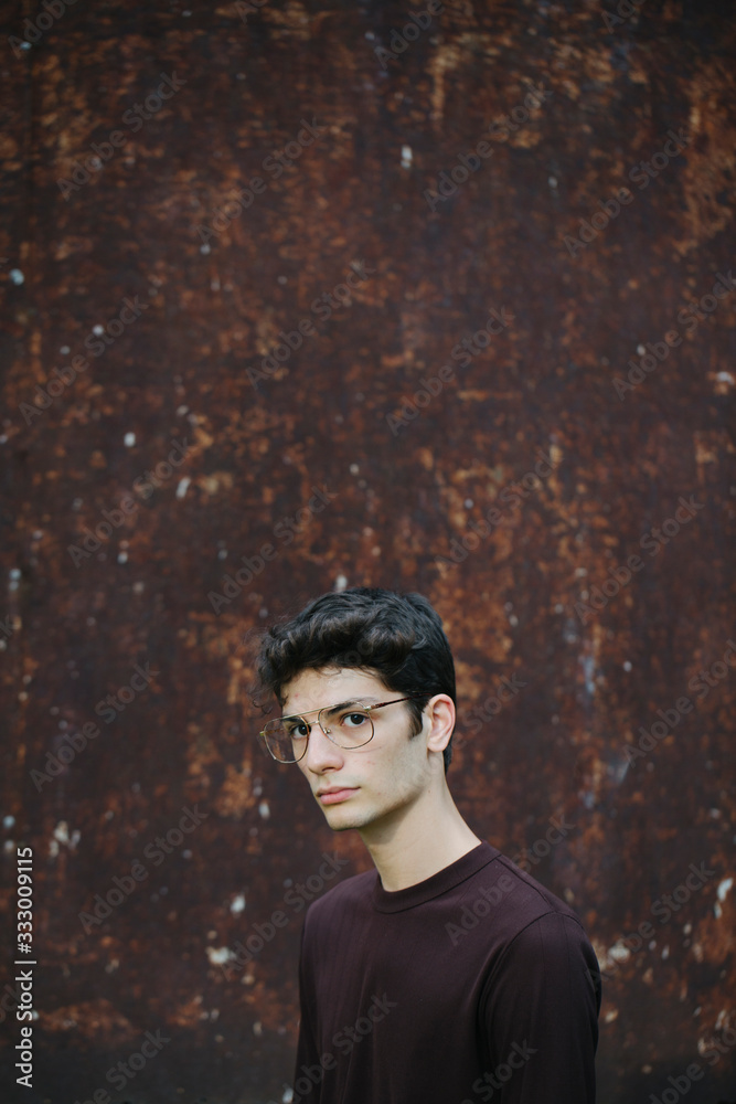 Serious young man with glasses looking at camera on rusty background Serious young man with glasses looking at camera on rusty background