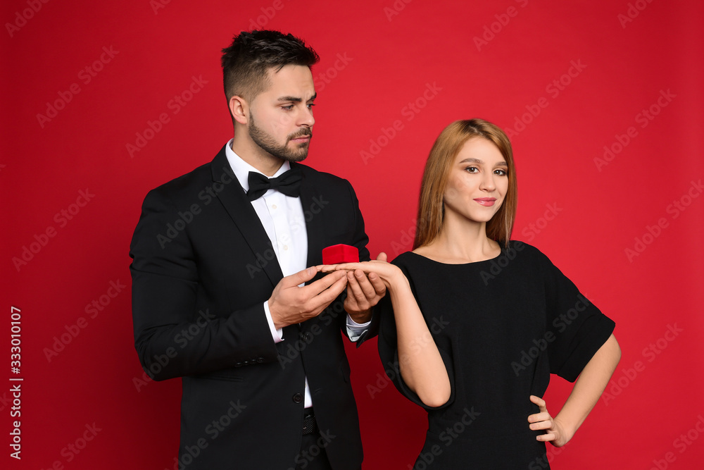 Young woman with engagement ring making marriage proposal to her boyfriend on red background