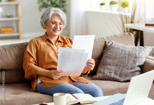 Happy elderly freelancer reading papers on sofa.