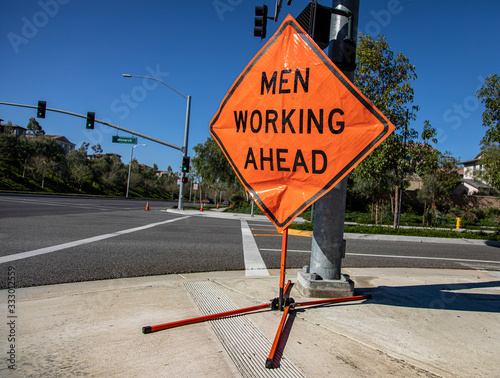Orange diamond shaped traffic control sign reading “Men Working Ahead” on street corner