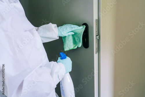 A person protected with safety clothing against a pandemic or virus, cleans and disinfects a portal of a house © Dani