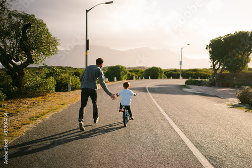 Rear view of father teaching his son to ride bicycle