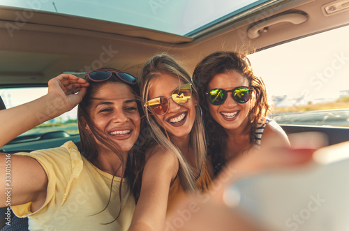 Three female friends enjoying traveling in the car. Sitting in rear seat and and making selfie. © Zoran Zeremski
