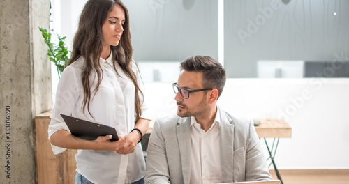 Young businesswoman and businessman discussing paperwork together in modern office.