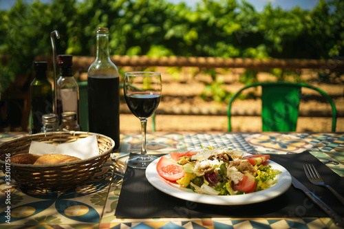 Mediterranean lunch in a farm restaurant, a glass, a bottle of wine and salad on a vineyard background