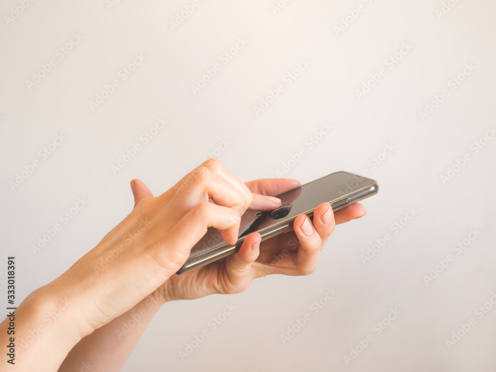 Fototapeta premium Female hands cleaning smartphone with sanitizer gel over bright gray background