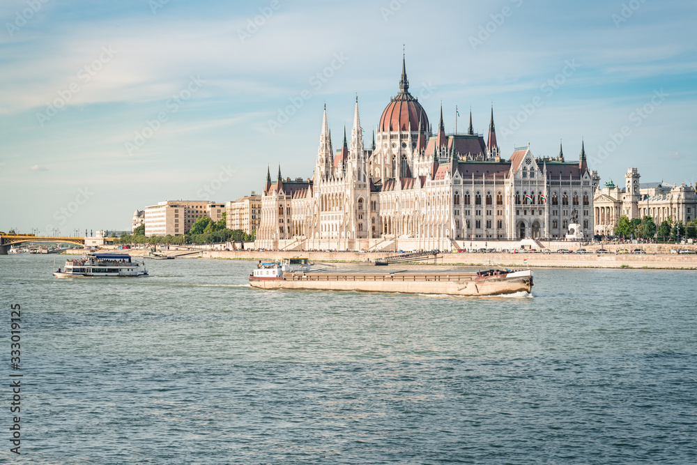 Obraz premium The Budapest Parliament at sunset. Boats passing by on Danube river, Hungary 2019