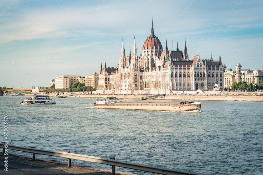 Fototapeta premium The Budapest Parliament at sunset. Boats passing by on Danube river, Hungary 2019