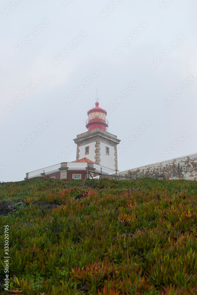 The lighthouse at Cape Cabo da Roca on a foggy day. A view of the rock and the lighthouse from bottom to top. The lighthouse at Cape Cabo da Roca on a foggy day. A view of the rock and the lighthouse from bottom to top.