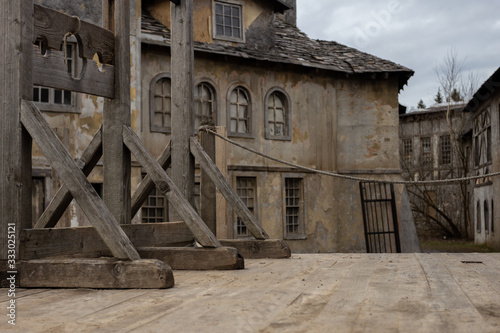 The photo shows part of a dark medieval or pirate town with a guillotine on a wooden platform. In the background, houses with broken windows, desolation and destruction as during the plague pandemic.
