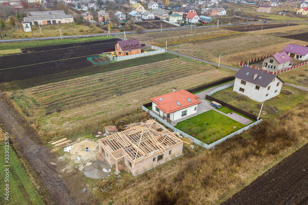 Top down aerial view of two private houses, one under construction with wooden roofing frame and another finished with red tiled roof.