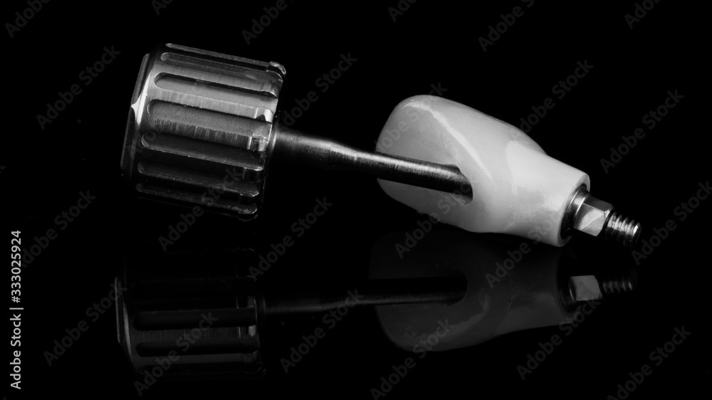 dental crown of front incisor made of ceramic and zircon, on black glass with a screwdriver in black and white style dental crown of front incisor made of ceramic and zircon, on black glass with a screwdriver in black and white style