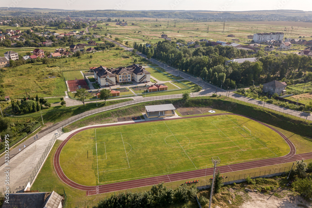 Aerial view of a football field on a stadium covered with green grass in rural town area.