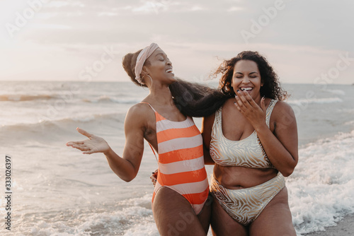 Two african american female friends swimming and laughing at the beach