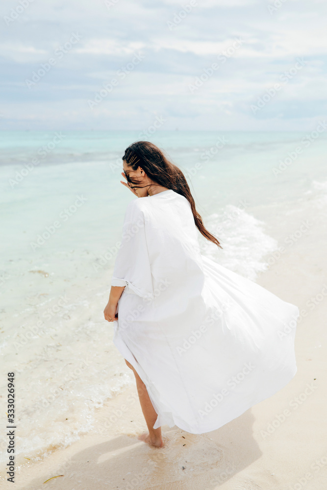 Woman in a dress walking in the empty beach Woman in a dress walking in the empty beach