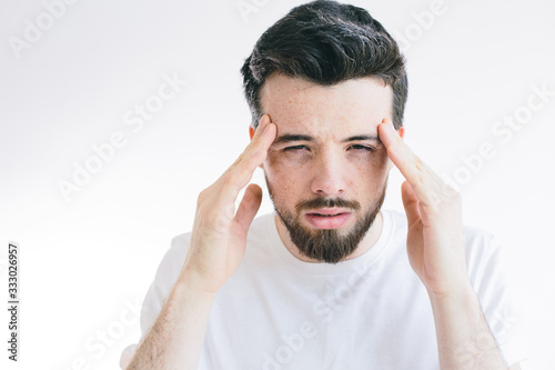 Young bearded man suffer from headache, Hold fingers on head and look on camera. Need pain relief or pill from ache. Stand alone isolated over background.