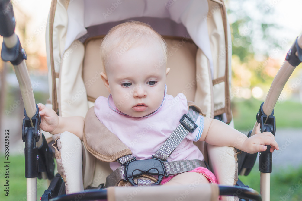 a small child is sitting in a pram strapped in and looking around in a city Park the face of a child close up a small child is sitting in a pram strapped in and looking around in a city Park the face of a child close up