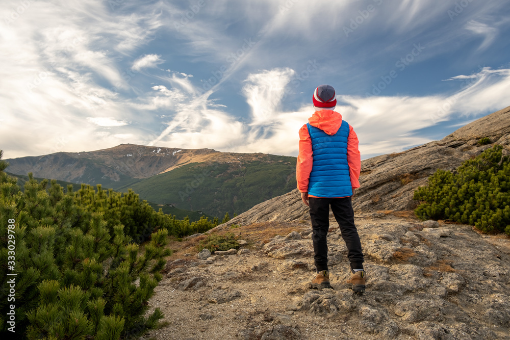 Young child boy hiker standing in mountains enjoying view of amazing mountain landscape.