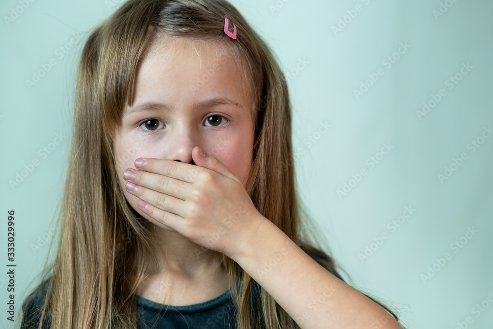 Close-up portrait of little child girl with long hair covering her mouth with hands. Close-up portrait of little child girl with long hair covering her mouth with hands.