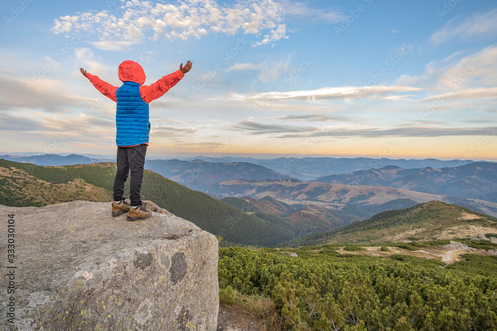 Young child boy hiker standing with raised hands in mountains enjoying view of amazing mountain landscape at sunset. Young child boy hiker standing with raised hands in mountains enjoying view of amazing mountain landscape at sunset.