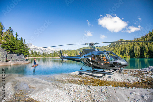 female paddle boards on lake next to her helicopter