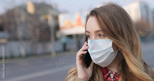 Portrait of young woman in medical face mask talking on a smartphone on the street. Coronavirus quarantine. Pandemic concept, coronavirus epidemic.