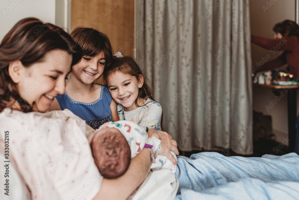 Side view of mother holding newborn son meeting siblings Side view of mother holding newborn son meeting siblings