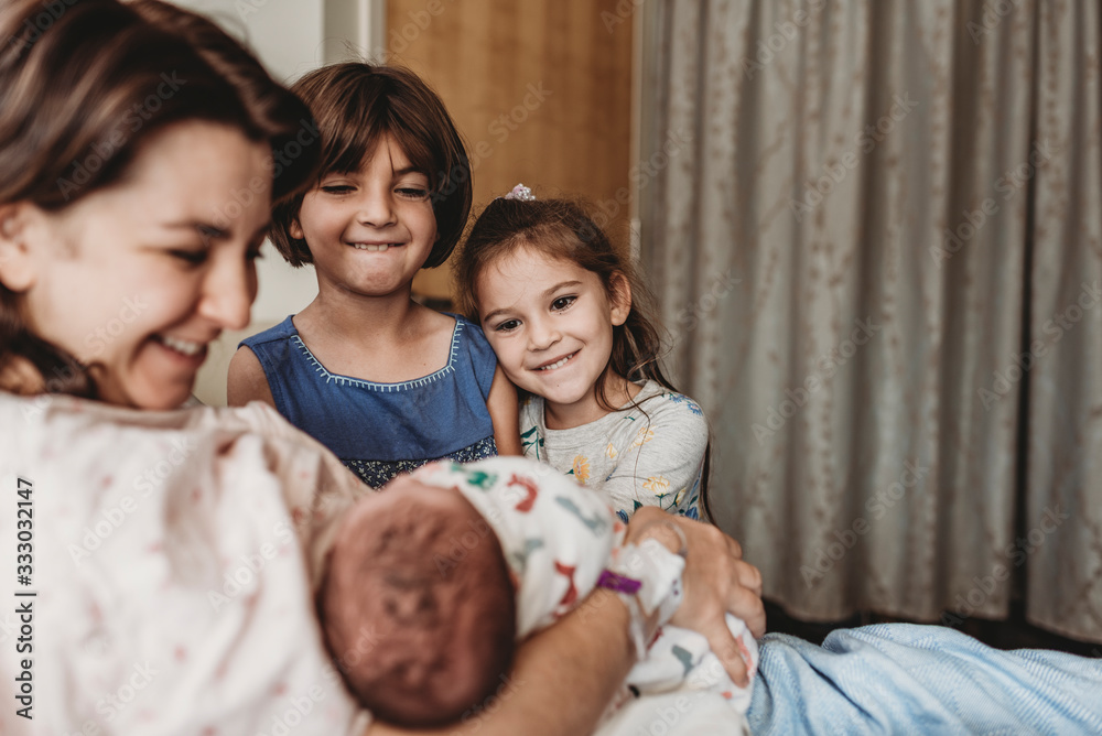 Side view of mother holding newborn son meeting siblings